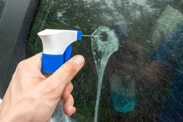 一只拿着塑料喷雾瓶的手溅到汽车的玻璃上 — 图库照片