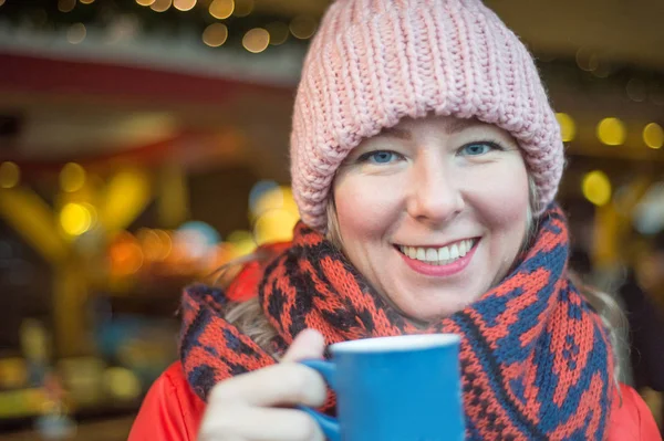 beautiful woman in scarf drinks mulled wine on christmas market