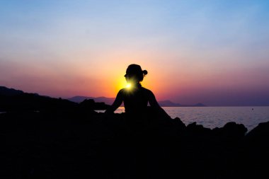 Gün batımında sahilde yoga yaparken genç bir kadın silüeti.