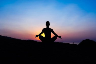 Gün batımında sahilde yoga yaparken genç bir kadın silüeti.
