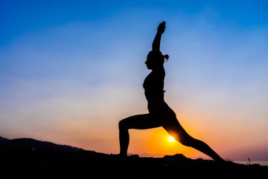 Gün batımında sahilde yoga yaparken genç bir kadın silüeti.