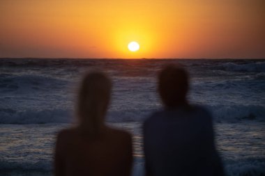 İki kız sahilde oturup gün batımını izliyor.