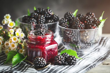 Olgun böğürtlen ve böğürtlen reçeli ahşap bir masa üzerinde. Koyu arka plan.