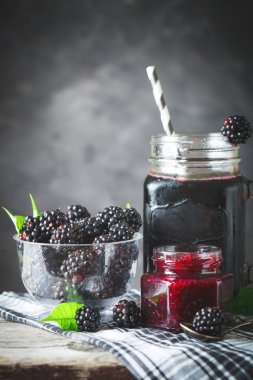 Olgun böğürtlen, böğürtlen suyu ve reçel ahşap bir masa üzerinde. Koyu arka plan.