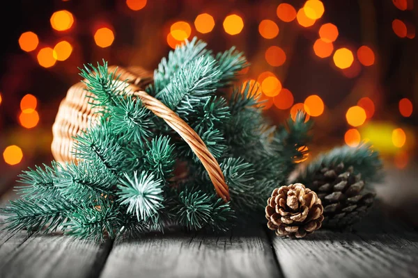 Καλά Χριστούγεννα και Ευτυχισμένο το νέο έτος. Καλάθι με τα κλαδιά του Χριστουγεννιάτικου δέντρου σε ένα ξύλινο τραπέζι για το ιστορικό της μια γιρλάντα. — Φωτογραφία Αρχείου