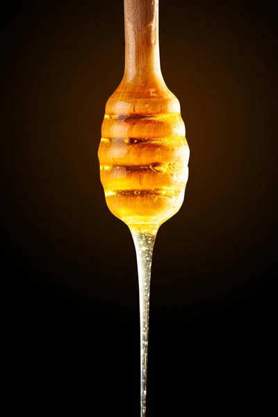 Honey with gold color flows down from a spoon, on a dark background. Healthy eating. Diet. Selective focus. — Stock Photo, Image