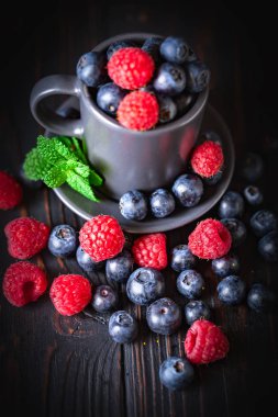 Ahududu ve yaban mersini karanlık bir arka plan üzerinde bir Fincan içinde. Yaz ve sağlıklı gıda konsepti. Seçici odak. Dikey.