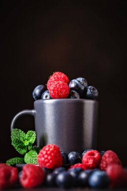 Ahududu ve yaban mersini karanlık bir arka plan üzerinde bir Fincan içinde. Yaz ve sağlıklı gıda konsepti. Kopyalama alanı ile arka plan. Seçici odak. Dikey.