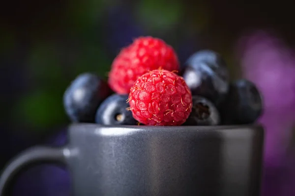 Raspberries and blueberries in a Cup on a dark background. Summer and healthy food concept. Selective focus. Horizontal. — Stock Photo, Image