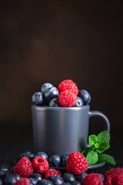 Ahududu ve yaban mersini karanlık bir arka plan üzerinde bir Fincan içinde. Yaz ve sağlıklı gıda konsepti. Kopyalama alanı ile arka plan. Seçici odak. Dikey.