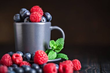 Ahududu ve yaban mersini karanlık bir arka plan üzerinde bir Fincan içinde. Yaz ve sağlıklı gıda konsepti. Kopyalama alanı ile arka plan. Seçici odak. Yatay.