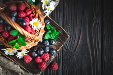 Ahududu ve yaban mersini papatya ile bir sepet içinde ve koyu bir arka plan üzerinde bırakır. Yaz ve sağlıklı gıda konsepti. Kopyalama alanı ile arka plan. Seçici odak. Düz yatıyordu.