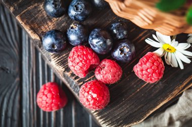 Ahududu ve yaban mersini papatya ile bir sepet içinde ve koyu bir arka plan üzerinde bırakır. Yaz ve sağlıklı gıda konsepti. Seçici odak. Düz yatıyordu.