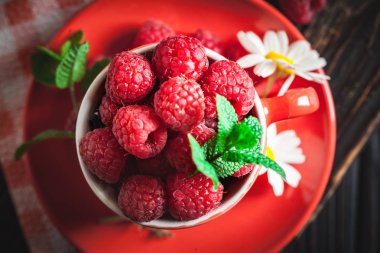 Papatya ile kırmızı bir fincan ahududu ve koyu bir arka plan üzerinde bırakır. Yaz ve sağlıklı gıda konsepti. Seçici odak. Düz yatıyordu.