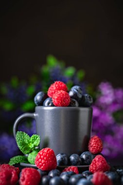 Ahududu ve yaban mersini karanlık bir arka plan üzerinde bir Fincan içinde. Yaz ve sağlıklı gıda konsepti. Kopyalama alanı ile arka plan. Seçici odak. Dikey.