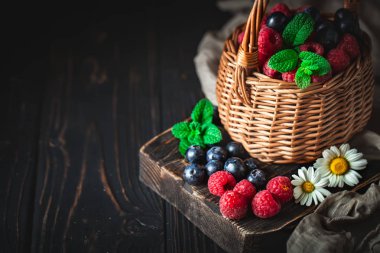 Ahududu ve yaban mersini bir sepetin içinde papatya çayı ve koyu arkaplanda yapraklar. Yaz ve sağlıklı gıda konsepti. Kopya alanı olan bir arkaplan. Seçici odak.