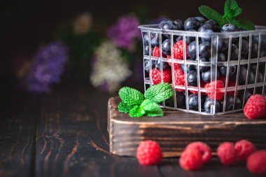 Ahududu ve yabanmersini sepetinde koyu bir arka planda. Yaz ve sağlıklı gıda konsepti. Kopya alanı olan bir arkaplan. Seçici odak.