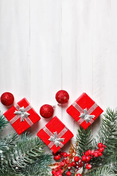 God jul och gott nytt år. Gåvor och fir-trädgrenar på en vit träbord. Selektivt fokus. Jul bakgrund. Lodrät. Ovanifrån. — Stockfoto