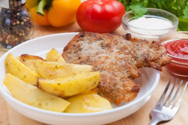 soslu ahşap bir Tahta üzerinde beyaz bir tabakpatates dilimleri ile domuz pirzolası. Sebzelerle dekore edilmiş