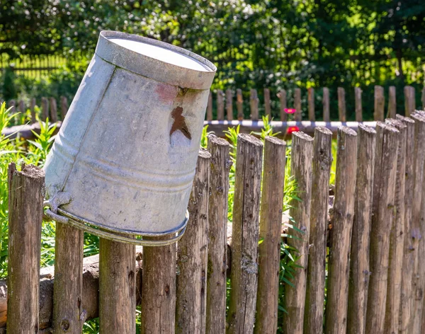Vintage tin bucket on the wooden fence of a vegetable garden