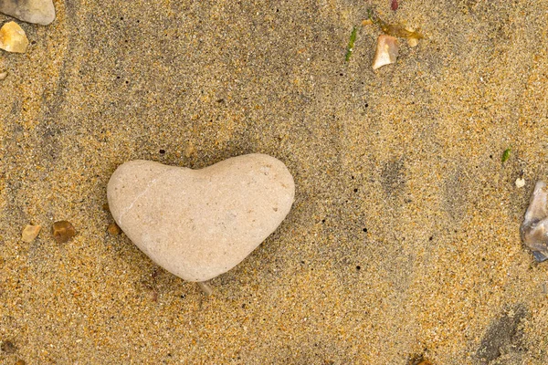 Close up de um seixo amarelo em forma de coração deitado em uma praia de areia no sul do Reino Unido — Fotografia de Stock