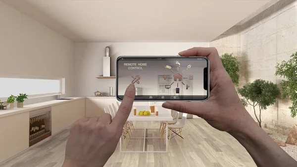 Remote home control system on a digital smart phone tablet. Device with app icons. Interior of minimalist white kitchen in the background, architecture design.