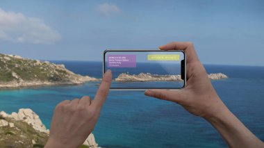 Augmented reality marketing and travel purpose concept. Hand holding smart phone use AR application to check information about the spaces around customer. Sardinia Italy, mediterranean sea. clipart