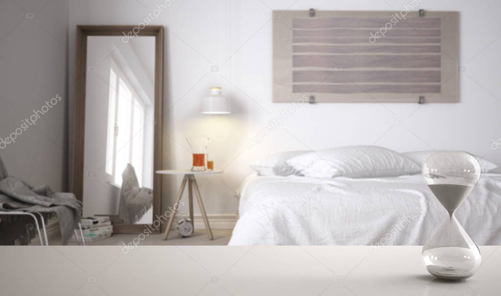 White table or shelf with crystal hourglass measuring the passing time over modern bedroom with double bed, architecture interior design, copy space background