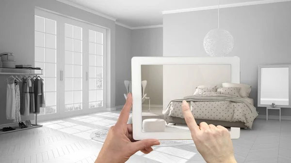 Augmented reality concept. Hand holding tablet with AR application used to simulate furniture and interior design products in real home, modern bedroom with double bed