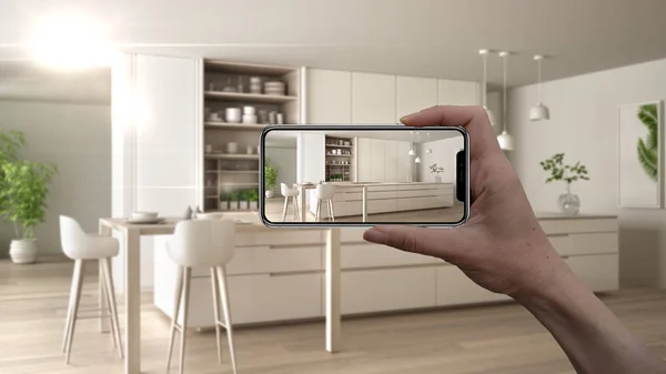 Hand holding smart phone, AR application, simulate furniture and interior design products in real home, architect designer concept, blur background, modern white and wooden kitchen