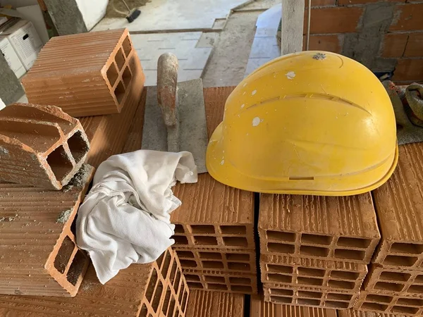 Builder lays red brick at a construction site, helmet, pair of gloves and spatula, work tools