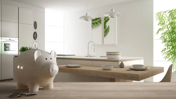 Wooden table top or shelf with white piggy bank with coins, modern white and wooden kitchen, expensive home interior design, renovation restructuring concept architecture