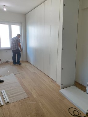 Marangozlar dolabın kapaklarını beyaz bir dolaba yerleştiriyor, dolapta yürüyorlar. Kısmen kurulu mobilyalar.