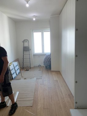 Marangozlar dolabın kapaklarını beyaz bir dolaba yerleştiriyor, dolapta yürüyorlar. Kısmen kurulu mobilyalar.