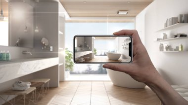 El ele tutuşan akıllı telefon, AR uygulaması, gerçek evdeki mobilya ve iç tasarım ürünleri, mimar tasarım konsepti, bulanık arka plan, küvetli minimalist banyo
