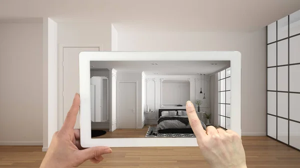 Augmented reality concept. Hand holding tablet with AR application used to simulate furniture and design products in empty interior with parquet floor, modern white and gray bedroom