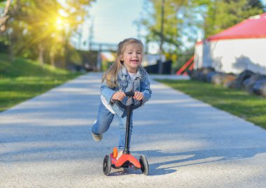 Küçük kız parkta bir scooter sürme