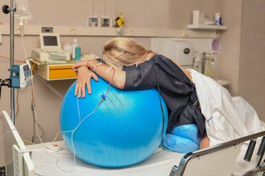 Woman during contractions on a blue fitness ball Parturition hospital clipart