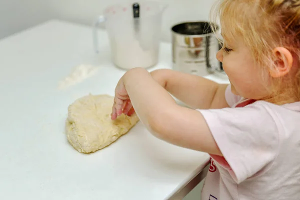 Little girl kneads dough in the kitchen