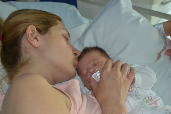 En mamma kysser hennes nyfödda bebis sova i sängen — Stockfoto