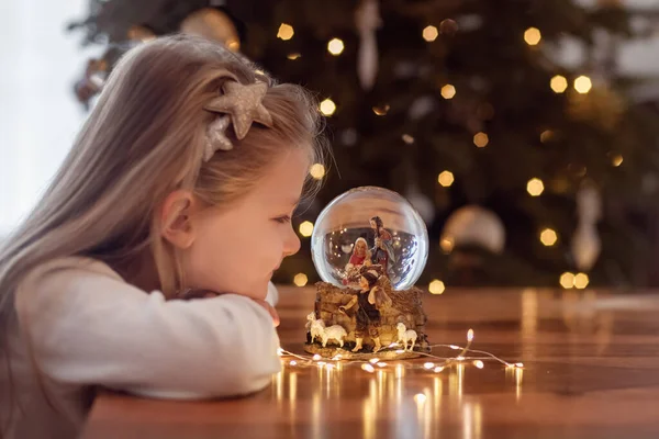 クリスマスツリー上のガラスボールにイエス キリストのネイティブのシーンとガラスボールを見て女の子 — ストック写真