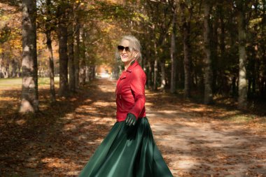 A happy sixty-year-old gray-haired woman strolls in the gardens or forest of Versailles