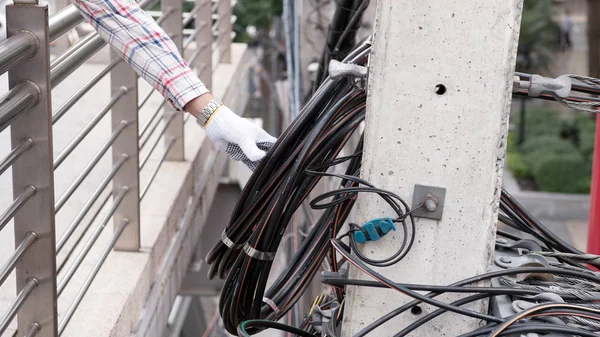 Hand of electrician tests electrical installations and wires on relectric pole outdoor.
