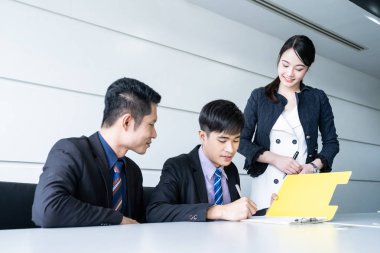 Tablo ve evrak ortağının imzalama ve karlı anlaşması yaptıktan sonra gülümseyerek oturan kendine güvenen iş adamı.