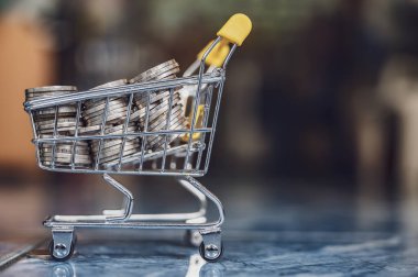 Sarı alışveriş arabasındaki para paraları soyut arkaplanı bulanıklaştırır.