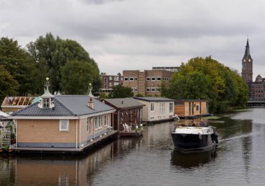 Vlaardingen, Rotterdam, Hollanda. Ağustos 2018: yat geleneksel evleri ile kanal boyunca Vlaardingen şehir bir bulutlu kiliseyle arka plan üzerinde su üzerinde yelken açtı