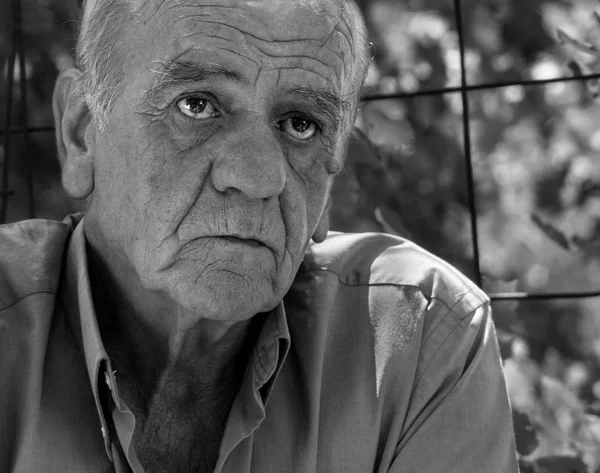 Closeup portrait of a serious old greek retired male who smokes a cigarette with a smile, in black and white