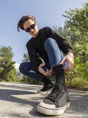 Kot pantolon ve spor ayakkabı içinde genç adam yolun ormanın içinde oturur