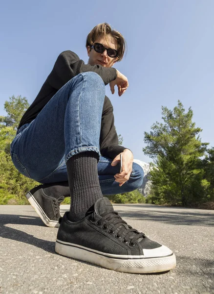 Young man in jeans and sneakers sits on the road in the woods