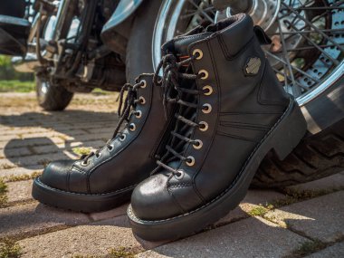 Motorlu botlar, bağcıklı, yakın plan, motosiklet tekerinin yanında duruyor.